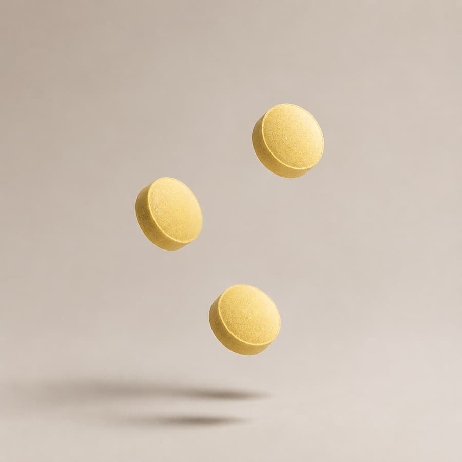 Three yellow Biotin and Minoxidil capsules floating against a warm greige background